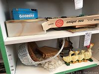 Shelf with vintage toy cars in original Milo Wheels box, cast iron Mother Goose door stop, duck coasters in rocking chair holder, white woven basket and wood baskets