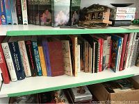 Shelf with an assortment of cookbooks and some miscellaneous items including DVDs and a miniature house model.