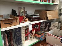 Photo of white shelving unit with boxes and items including multiple bibles, games, USS Constitution model, drawer pulls, and assorted books.