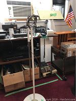Tall white floor lamp with round base and visible cord wrapped on pole.