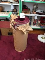 Area rug laid flat in room with visible wear and deep red rolled-up runner wrapped in paper standing upright on it