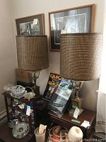 Pair of vintage brass lantern style table lamps with brown woven shades shown on side tables surrounded by other miscellaneous items.