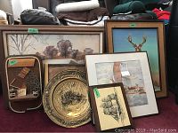 Overall view of framed wall art and decorative items against a wall including large 22x28 landscape, ship prints, deer illustration, metal plate, and mixed media plaque.
