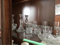 Crystal stemware, decanter, candlesticks, and bowls displayed inside a wooden cabinet with glass shelves.