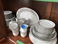 Full set of Crown Ming fine china displayed on shelf, includes various plates, cups, and two large serving platters, one cup marked broken with blue tape.