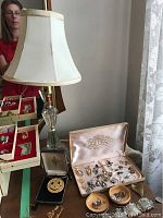 Photo of vintage cameo rings, earrings, costume jewelry in boxes, displayed on wood table with crystal lamp and fabric shade nearby.