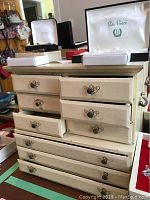 Full view of off-white wooden jewelry box with multiple drawers and decorative metal handles