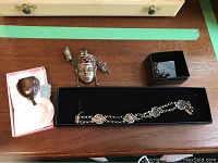 All items laid out on wooden surface: bracelet, Far East brooch, earrings in box, and teething ring in pink box.