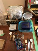 Lot showing assortment of watches with varied bands, buttons box, sewing supplies container, and some watch accessories on wooden table.
