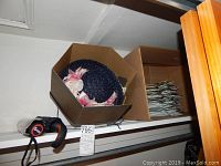 Vintage navy ladies' spring hat decorated with pink and white fabric flowers inside original brown box, next to a box full of clothes hangers.