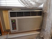 Front view of the Zenith ZW6500R window air conditioner installed in a window with digital temperature display showing 65°F, horizontal vents, and surrounding window frame and drapery.