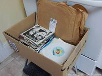 Box of multiple vintage vinyl records, mostly in paper sleeves and some original album covers.