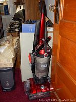 Full view of the red Hoover Wind Tunnel upright vacuum cleaner with hose and accessories attached, standing upright on red carpet.