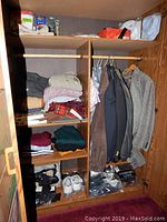 View of wardrobe shelves with folded clothes including sweaters, shirts, scarves, and shoes on bottom shelf