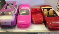 Four Barbie vehicles displayed: VW Van in pink and purple on left, two red Barbie sports cars in middle, pink Mustang convertible on right