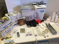 Wii console and accessories spread out including games, remotes, nunchuks, charging station, and battery packs