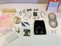Full assortment of jewelry including earrings, pin, bracelet, and storage pouches. Jewelry pieces vary from vintage to new, some are tarnished.