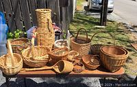 Photo of a table holding various wicker baskets outside, showing a variety of shapes and sizes with some having handles and others not.