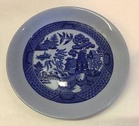 Top view of a Blue Lune Ware plate showing blue and white pattern with pastoral and architectural scenes.