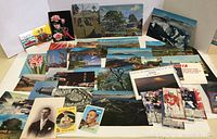 Overall view of the assortment of vintage postcards laid flat, including landscapes, flower postcards, sepia toned portrait, and sports cards on the right