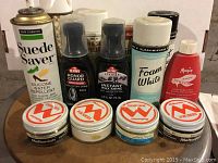 Photo showing various shoe polish tins and shoe care sprays including Meltonian, Kiwi Honor Guard, Kiwi Instant Wax Shine, Suede Saver, Foam White, and Magia bottles.