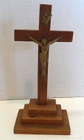 Photo of vintage wood and metal crucifix standing upright, showing the figure of Jesus and INRI plaque at the top, mounted on a tiered wooden base.