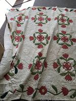 Photo of antique quilt with floral patterns in red and green on beige background, showing wear and fabric condition.