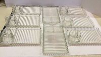 Full set of 8 Anchor Hocking clear glass trays with matching coffee mugs, all displayed together.