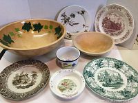 Wide shot showing all wooden bowls and collectible plates in the lot, including decorative bowls and assorted plates with various vintage and collectible designs.
