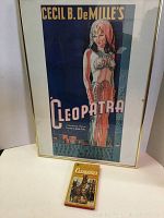 Framed reproduction movie poster of Cecil B. DeMille's 1934 film Cleopatra starring Claudette Colbert, displayed alongside the paperback book.
