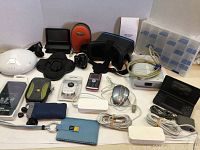 Full view photo of the mixed electronics lot showing many items including VR headset, GPS device, mobile phones, cables, headphones, and cases arranged on a white background.