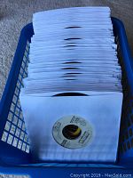 Photo showing a blue basket filled with approximately 101 vinyl 45 RPM records in white sleeves.