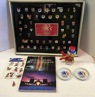 Framed sponsor pin set, souvenir program, unopened sticker set, figurine and two coasters shown together