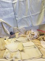 Overview of assorted antique and vintage linens spread out on a surface, showing some folded and some laying flat with lace and embroidered details visible.