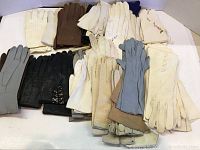 Grouped display of multiple assorted antique gloves showing variety in color and material, mainly light and neutral shades with some black and blue pairs.
