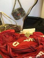 Photo showing all bags and wallet in the lot including Wilson racket bag (red), messenger bag (black), small reptile skin shoulder bag, white floral clutch, brown handbag, beaded wallet visible.