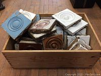 Wood crate filled with a variety of painted vintage wood architectural rosettes, showing chipped paint and some damage.