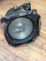 Vintage square spotlight light showing front view with circular textured glass lens within metal frame with chipped paint.