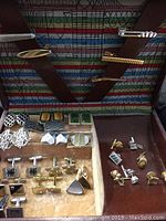 Overview of cufflinks, tie clips, and tie pins arranged inside Buxton box with colorful interior lining.