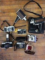 Overview of seven vintage cameras and accessories laid out on wooden floor