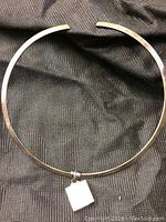 Full view of the circular sterling silver choker on dark fabric background showing the rigid metal band.