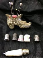 Photo showing the porcelain shoe pin cushion with four pins and six thimbles of various materials and designs.