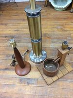 Lot showing three table lamps on wood floor: brass lamp, teak lamp, and wood design lamp.