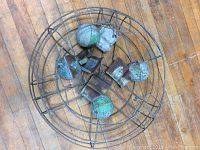 Circular metal fan cage with green and rusted metal spheres and metal brackets inside on wood floor