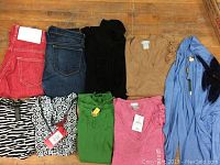 Overview of all clothing items laid out on wooden floor including jeans, tops, sweaters, and shirts.