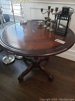 Photo showing entire round wooden table with various items on top (not included). The table is dark brown with a single pedestal and four feet supports.