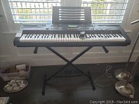 Full view of Casio keyboard on X-style metal stand in front of window showing overall size and condition.