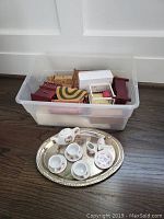 Plastic bin containing various wooden dollhouse furniture pieces including chairs, tables, benches, and small woven rug.