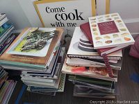 Photo of two stacks of cookbooks, titles visible include 'España,' 'The Cheese Companion,' and 'Scotch.'