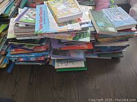 Pile of children's books stacked on the floor showing various titles and covers.